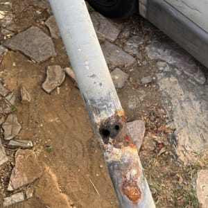 צינור חלוד עם חורים על רקע קרקע ואבנים
