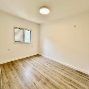 חדר עם רצפת עץ, קירות לבנים ותאורה עגולה בתקרה.