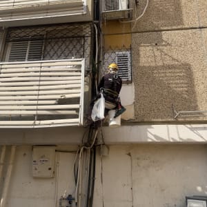 אינסטלטור המבצע עבודה בגובה בסנפלינג על קיר חיצוני של בניין