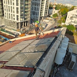 עובד על גג עם קסדה וכלי עבודה, בניינים ברקע