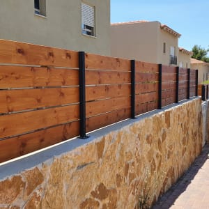 גדר עץ עם עמודי מתכת על קיר אבן