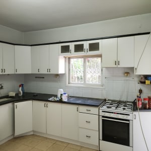 מטבח עם ארונות לבנים, כיריים וגז, חלון עם סורגים