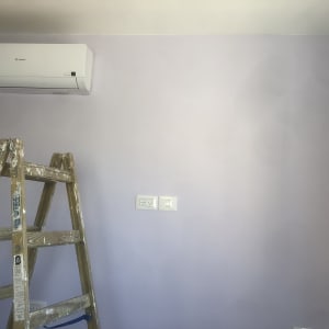 סולם עץ עם כתמי צבע ליד קיר צבוע