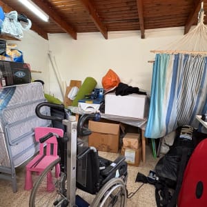 חדר עם חפצים שונים, כולל כיסא גלגלים ומזרנים.