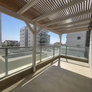 מרפסת עם פרגולה ומעקה זכוכית בבניין מגורים