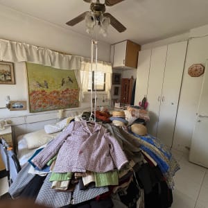 חדר עם בגדים על המיטה, טלפון שולחני, ציור על הקיר