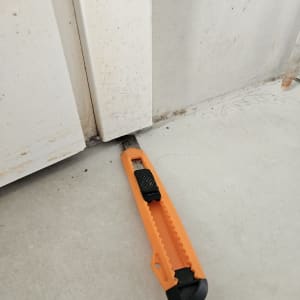 סכין חיתוך כתום ליד דלת לבנה על רצפה אפורה