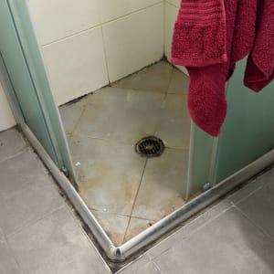 מקלחת עם רצפה מלוכלכת ומגבת אדומה תלויה