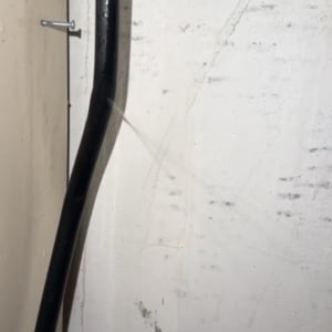 צינור שחור על קיר לבן עם סימני רטיבות