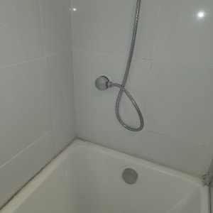 אמבטיה עם צינור מקלחת על קיר אריחים לבנים