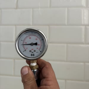 מד לחץ מים מוחזק ביד על רקע קיר אריחים לבנים