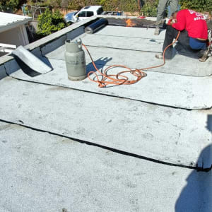 עובדים אוטמים גג עם יריעות ביטומניות ומבער גז