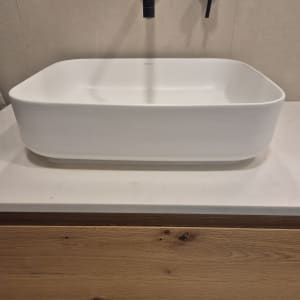 כיור לבן עם ברז שחור על רקע עץ