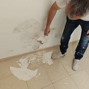 אדם משפץ קיר עם שפכטל ופסולת על הרצפה