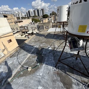 גג עם ציפוי איטום ומיכלי מים על רקע בניינים