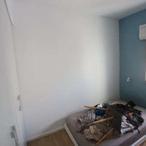 חדר עם קיר לבן ומיטה עם בגדים וכלים על המזרן