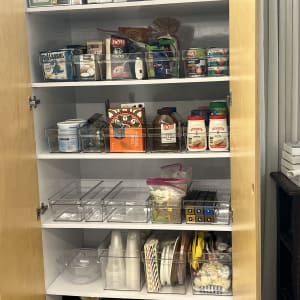 ארון עם מוצרי מזון וארגון ביתי, כולל קופסאות פלסטיק ומצרכים שונים.