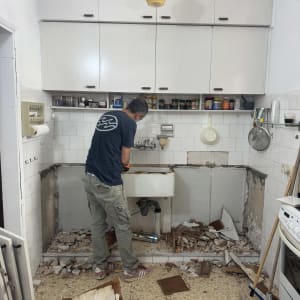 אדם עובד על שיפוץ מטבח עם כיור שבור