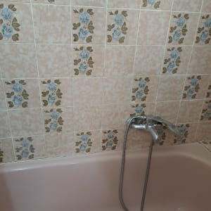 אמבטיה ורודה עם ברז ישן על רקע אריחים פרחוניים