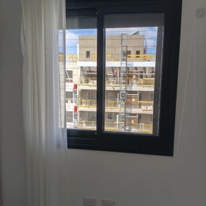 חלון עם וילון לבן ונוף לבניין בבנייה