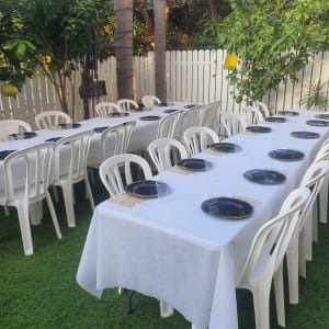 שולחנות עם מפות לבנות, כיסאות פלסטיק וצלחות שחורות