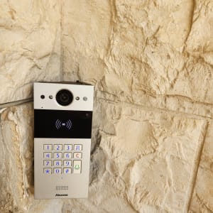 אינטרקום עם מצלמה ומקשים מוארים על קיר אבן