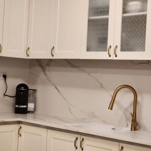 מטבח עם ארונות לבנים, ברז זהב ומכונת קפה שחורה