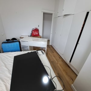 חדר עם מזוודה כחולה, ארון לבן וטלוויזיה על מיטה.