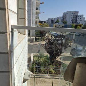 מעקה זכוכית במרפסת עם נוף לבניינים ועצים