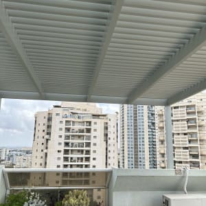 פרגולה מאלומיניום על רקע בניינים גבוהים.