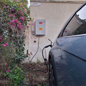 רכב חשמלי מחובר לעמדת טעינה על קיר חיצוני