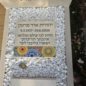 מצבה מעוצבת עם מילוי חלוקי נחל לבנים, לוח זיכרון ועיטור פסיפס צבעוני