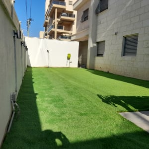 דשא סינתטי בחצר עם צינור השקיה על הקיר