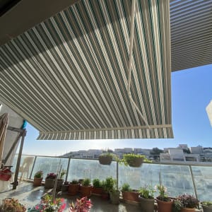 סוכך פסים ירוק לבן על מרפסת עם עציצים