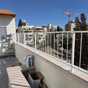 מעקה לבן על מרפסת עם נוף עירוני ועגורן ברקע