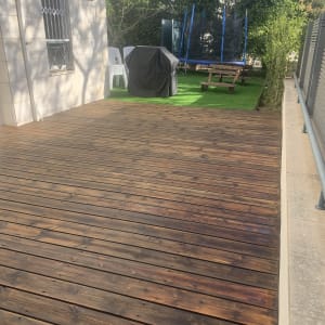 דק עץ חום ליד גינה עם דשא סינתטי