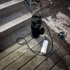 משאבה שחורה עם כבל על רצפת עץ ליד מדרגות