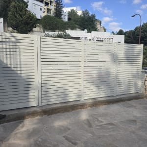 גדר אלומיניום לבנה בחצר עם רקע של עצים ובניינים