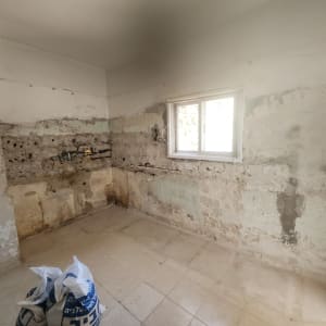 קירות חשופים עם סימני טיח, חלון, שקי חומרי בניין