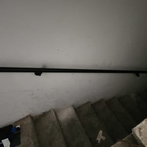 מעקה שחור מותקן על קיר מדרגות אפור