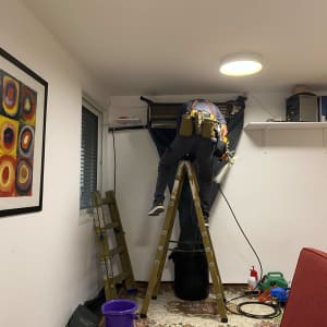 טכנאי עובד על מזגן על סולם בחדר