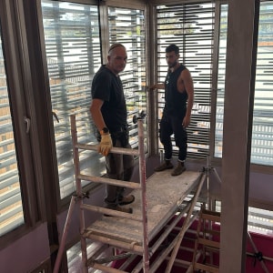 שני אנשים על פיגום ליד חלונות זכוכית גדולים