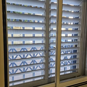 תריסים לבנים על חלון עם מסגרת מתכת