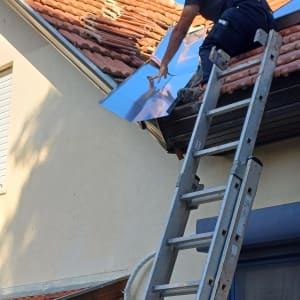 אדם על סולם מתקין לוחות מתכת על גג רעפים