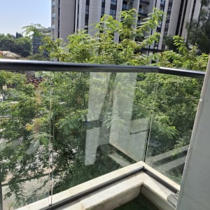מעקה זכוכית במרפסת עם נוף לעצים ובניינים