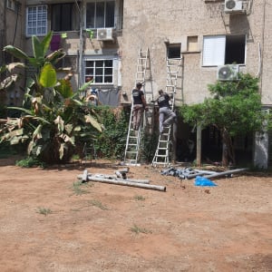 שני אנשים על סולמות מתקנים צינורות ליד בניין