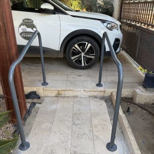 מכונית חונה ליד מעקה מתכת על שביל מרוצף