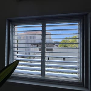 חלון עם תריסים ונוף חיצוני של בית ועצים