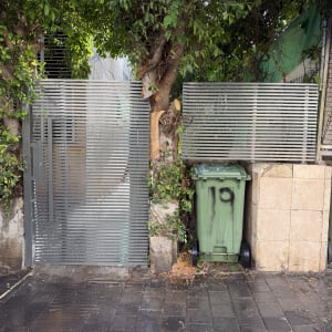שער אלומיניום ליד עץ ופח אשפה ירוק