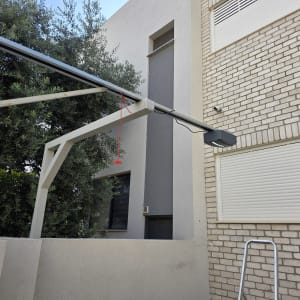 שער חשמלי עם מנוע ומבנה מתכת ליד בניין לבנים